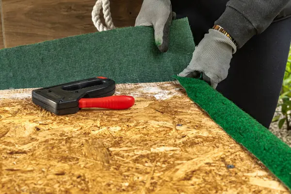 Yapay çimenleri ve yapay sarmaşık yapraklarını çivileyerek tahta bir tahtaya raptiye ve metal zımbalarla çivileyerek eski bir kapıyı yeniliyordu.