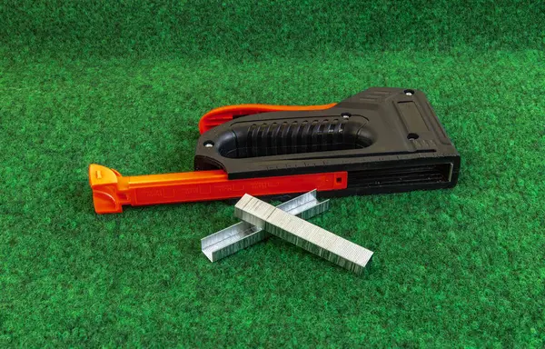 Yapay çimenleri ve yapay sarmaşık yapraklarını çivileyerek tahta bir tahtaya raptiye ve metal zımbalarla çivileyerek eski bir kapıyı yeniliyordu.