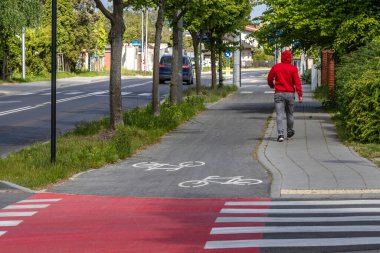 Kırmızı spor kazaklı bir adam kaldırım boyunca yürür bisiklet yolu boyunca ve kırmızı yaya geçidinde