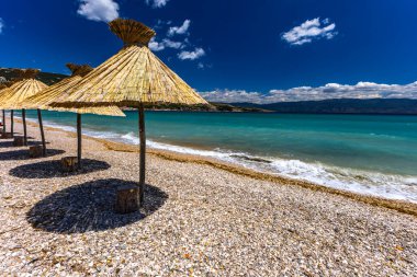 KRK adasındaki Baska plajında güneş gözlüğü, Hırvatistan 'da turizm sezonuna hazırlık, beac' ta şemsiye kurma