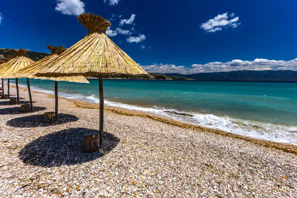 KRK adasındaki Baska plajında güneş gözlüğü, Hırvatistan 'da turizm sezonuna hazırlık, beac' ta şemsiye kurma