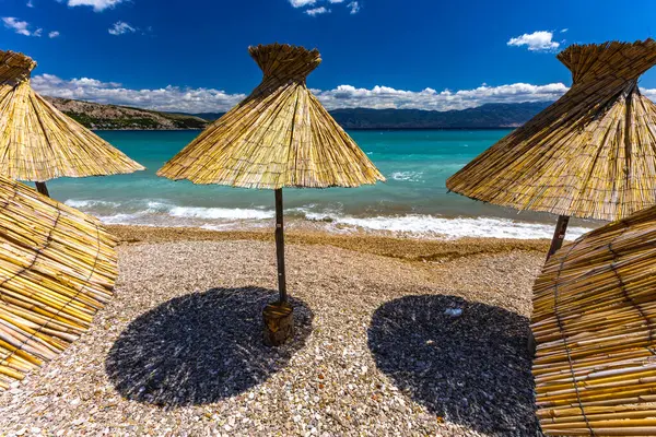 KRK adasındaki Baska plajında güneş gözlüğü, Hırvatistan 'da turizm sezonuna hazırlık, beac' ta şemsiye kurma