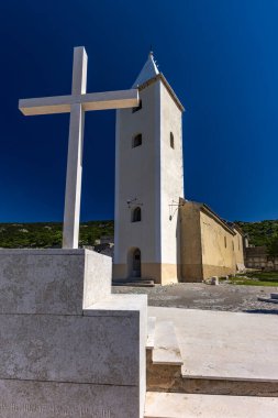 St. John Kilisesi, beyaz haç, çan kulesi, tepedeki mezarlık, KR adasındaki Baska kasabasının manzarası.