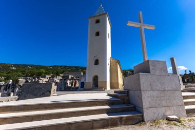St. John Kilisesi, beyaz haç, çan kulesi, tepedeki mezarlık, KR adasındaki Baska kasabasının manzarası.