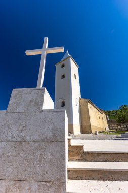 St. John Kilisesi, beyaz haç, çan kulesi, tepedeki mezarlık, KR adasındaki Baska kasabasının manzarası.