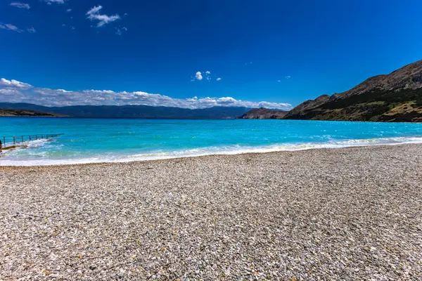 KRK adasındaki Baska 'daki boş çakıl taşı plajı, tatil sezonundan önce Hırvatistan' ın Adriyatik Denizi 'nde masmavi su