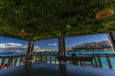 KRK adasındaki Baska körfezindeki gök mavisi suyun manzarası bir restoranın penceresinden, sahil şeridinin ilk hattındaki restoran, Bask 'ın merkezi.