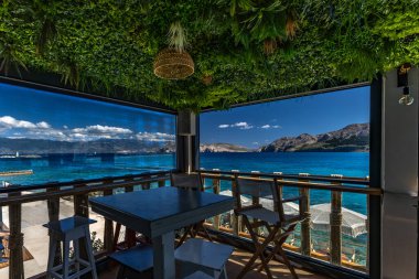 KRK adasındaki Baska körfezindeki gök mavisi suyun manzarası bir restoranın penceresinden, sahil şeridinin ilk hattındaki restoran, Bask 'ın merkezi.