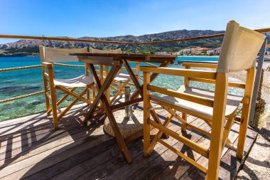 Hırvatistan 'ın Baska kentindeki Adriyatik Denizi' nde KR adasındaki bir restoranın verandasında tahta masa ve sandalyeler