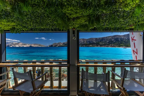 KRK adasındaki Baska körfezindeki gök mavisi suyun manzarası bir restoranın penceresinden, sahil şeridinin ilk hattındaki restoran, Bask 'ın merkezi.