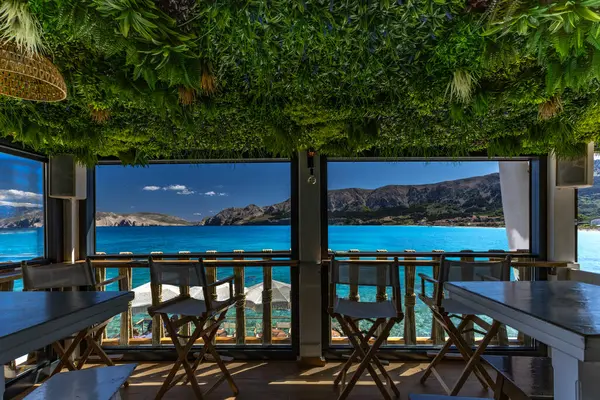 KRK adasındaki Baska körfezindeki gök mavisi suyun manzarası bir restoranın penceresinden, sahil şeridinin ilk hattındaki restoran, Bask 'ın merkezi.