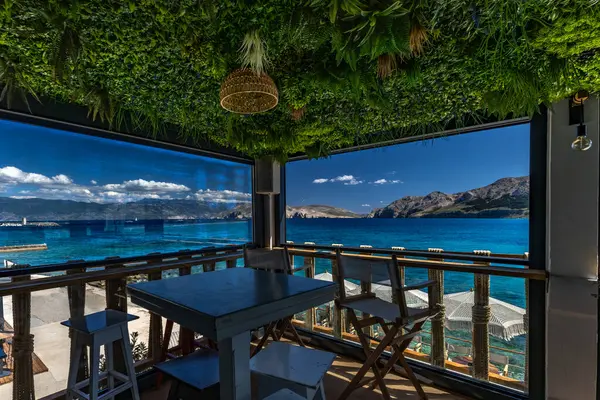 KRK adasındaki Baska körfezindeki gök mavisi suyun manzarası bir restoranın penceresinden, sahil şeridinin ilk hattındaki restoran, Bask 'ın merkezi.