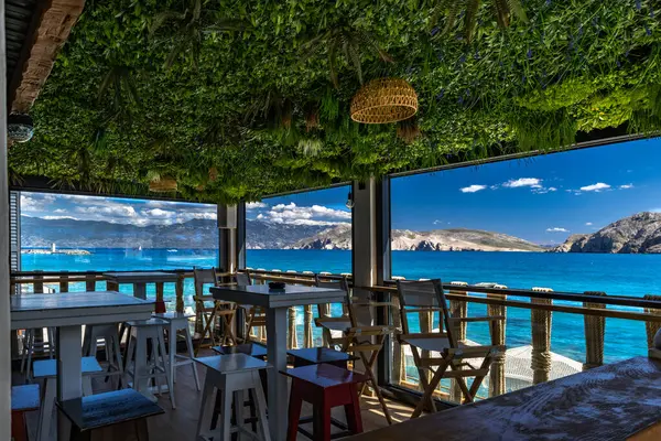 KRK adasındaki Baska körfezindeki gök mavisi suyun manzarası bir restoranın penceresinden, sahil şeridinin ilk hattındaki restoran, Bask 'ın merkezi.