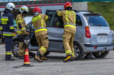İtfaiyeciler kazadan sonra bir arabanın gövdesini kesiyorlar, bir yolcuyu hurdaya dönmüş arabadan çıkarıyorlar, arabanın kapısını söküyorlar.