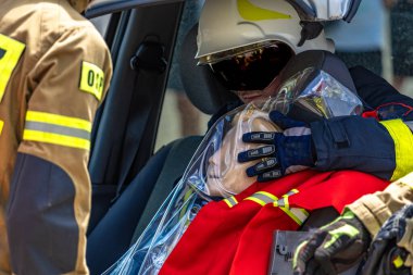 İtfaiye gösterisinde, bir itfaiyeci eldivenli bir mankeni korurken diğer kurtarıcılar kazadan sonra bir araba gövdesini kestiler.