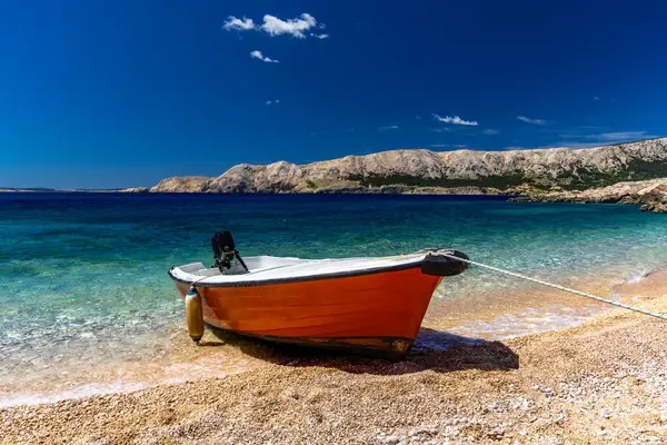Jablanova Sahili, turuncu balıkçı teknesi, Hırvatistan 'ın KRK adasındaki Adriyatik Denizi ve Velebit Dağları' nın zeminine karşı boş bir plajın kıyısında durdu.
