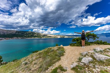 Bir kadın, Baska 'daki sahilden Bag Dağı' na yürürken yazıyor. Şehrin yukarıdan görünen manzarası, Bask sahilinin yanındaki koyu masmavi su.