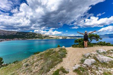 Bir kadın, Baska 'daki sahilden Bag Dağı' na yürürken yazıyor. Şehrin yukarıdan görünen manzarası, Bask sahilinin yanındaki koyu masmavi su.