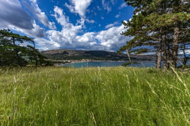 Açıklıkta yeşil çimenler, Baska kasabası yakınlarındaki bir patikada dinlenme, körfez ve şehir manzarası