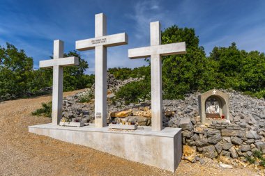 Punat tepesindeki Üç Haç Sığınağı, tapınağa dik kayalık bir yoldan giriş, KRK 'daki Punat kasabasının manzarası.