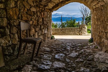 Vrbnik 'teki eski kasabanın duvarlarının altından geçmek, eski ahşap bir sandalye, turistler için dinlenme yeri.
