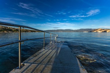 Adriyatik Denizi 'ne çakıl taşı plajından direk olarak engelliler için beton bir rampa ve güvenlik rayı ile giriliyor.