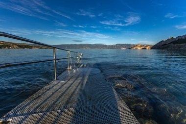 Adriyatik Denizi 'ne çakıl taşı plajından direk olarak engelliler için beton bir rampa ve güvenlik rayı ile giriliyor.