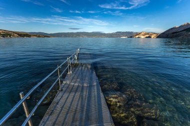 Adriyatik Denizi 'ne çakıl taşı plajından direk olarak engelliler için beton bir rampa ve güvenlik rayı ile giriliyor.