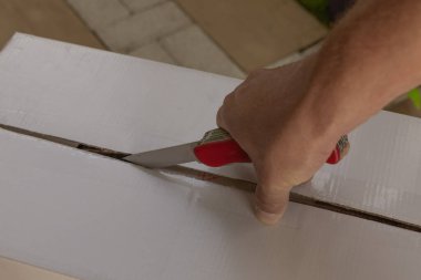 Bir adam elinde keskin bir bıçak tutar ve bir paketin güvenlik bandını keser ve kutuyu açar.