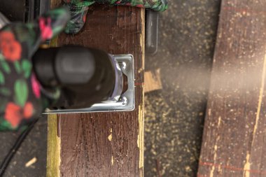 Renkli koruyucu eldivenler giyen bir kadın elektrikli yapboz kullanarak bahçede tahta kesiyor. Bahçe güvertesi için tahta kesmek, veranda ya da bahçe pergola yapmak.