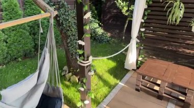 Evin önündeki bahçede bir dinlenme alanı, ahşap bir veranda, bir hamak, sallanan bir salıncak, terasta tahta ve çiçeklerden yapılmış bir pergola.