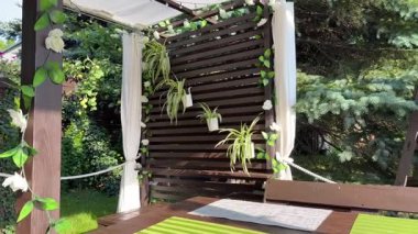 Evin önündeki bahçede bir dinlenme alanı, ahşap bir veranda, bir hamak, sallanan bir salıncak, terasta tahta ve çiçeklerden yapılmış bir pergola.