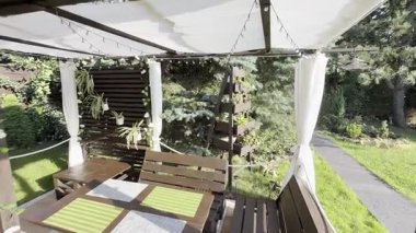 Evin önündeki bahçede bir dinlenme alanı, ahşap bir veranda, bir hamak, sallanan bir salıncak, terasta tahta ve çiçeklerden yapılmış bir pergola.