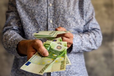 Genç bir adam, mavi şık gömlekli evli bir adam, elinde 100 euro banknot tutuyor, adam parayı karısına veriyor.