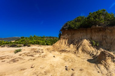 Engebeli kayalık zemin, yeşil çalılar, çam ağaçları ve dağınık bulutlu dramatik bir gökyüzü altında vahşi bitki örtüsü barındıran Akdeniz manzarasının güzel panoramik manzarası. Sahne sakin mavi bir denize bakıyor. Uzakta dağlar var.