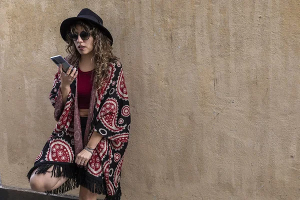 Young latina woman with curly hair, hat, sunglasses, talking on her cell phone