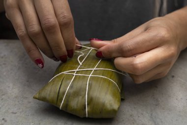 Kadının elleri hallaka ya da muz yaprağına tamale bağlıyor. Geleneksel yemek.