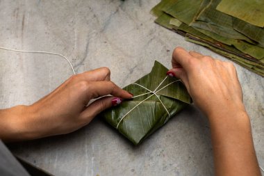 Woman's hands tying a hallaca or tamale in a banana leaf. Traditional food clipart