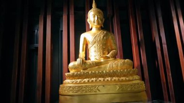 Altın Buda heykeli ahşap panellerin önünde duruyor.