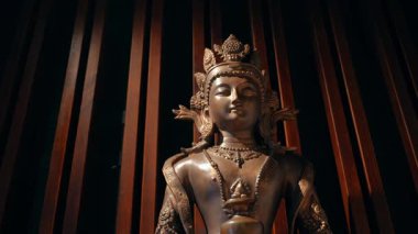 Tahta panellerin karşısında duran bronz Buda heykeli