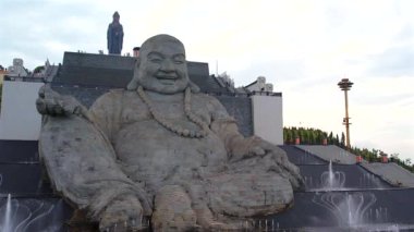 Büyük taş Buda heykeli dışarıda oturmuş huzur içinde gülümsüyor.