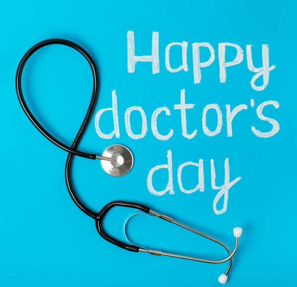 Doctor\'s day greeting card with stethoscope on blue background. Flat composition. Top view.