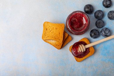 Reçelli tost ekmeği. Bir kavanoz yabanmersini reçeli. Masada kahvaltıda verilen tatlı reçelli lezzetli tost. Dokulu arka planda nefis tostlar. Mesaj için yer var. Kopyalamak için yer.