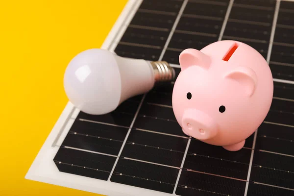 Flat lay composition with solar panel, led lamp and piggy bank on yellow background. The concept of saving money and clean energy. The concept of ecology and sustainable development.
