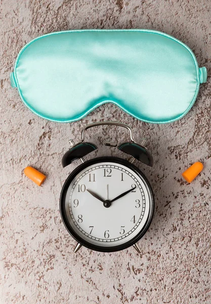Sleeping mask, alarm clock and earplugs on a colored background. The concept of rest, sleep quality, good night, insomnia and relaxation. View from above. flat lay