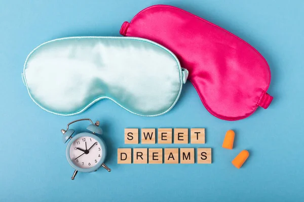 Sleeping mask, alarm clock, pills, ear plugs and the inscription SWEET DREAMS on a blue background. The concept of rest, sleep quality, good night, insomnia and relaxation. View from above. flat lay