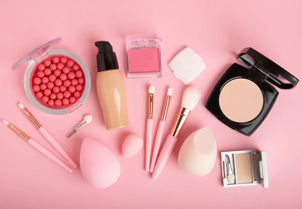 Beauty blender, foundation, concealer, blush,powder and makeup brushes composition on a pink background. Makeup artist concept, copy space. Applying facial cosmetics. Visagis.