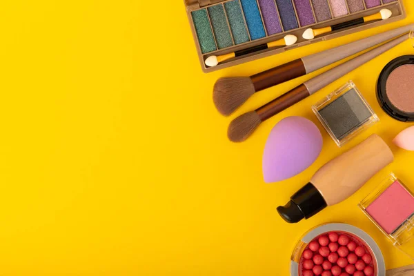 Beauty blender, foundation, concealer, blush,powder and makeup brushes composition on yellow background. Makeup artist concept, copy space. Applying facial cosmetics. Visagis.