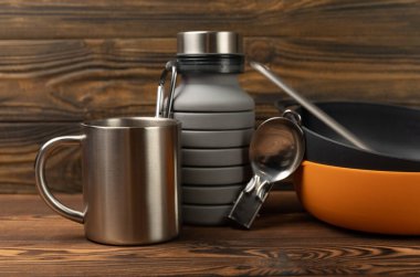 Kahverengi desenli arka planda seyahat ekipmanları. EDC hazır. Düz plan. Kamp tabağı, bardak, şişe, kaşık ve pusula..