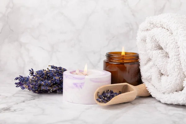Lavender flowers and scented candle. The concept of spa, beauty and health salon, skin care cosmetics. Natural cosmetics.Aroma procedures. Closeup on white marble background.